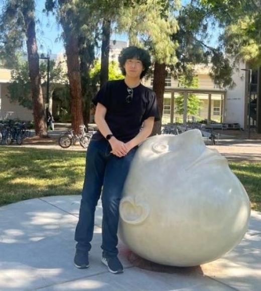 A person in a black shirt stands next to a large, rounded sculpture resembling a head.