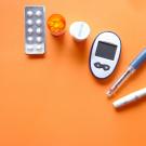 Glucose meter, lancet and insulin pens with pills and bottle on orange background